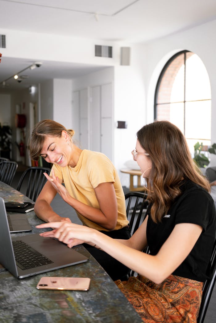 Home Two women engaged in a collaborative discussion at a modern office setting over laptops.
