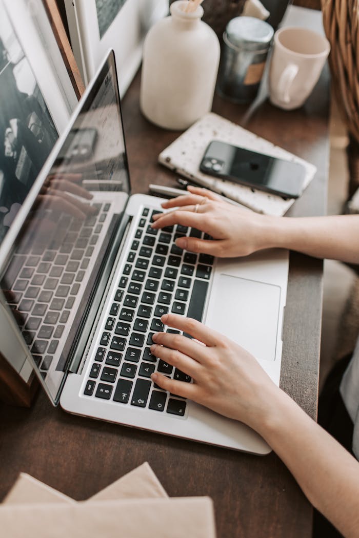 Home From above of unrecognizable woman sitting at table and typing on keyboard of computer during remote work in modern workspace
